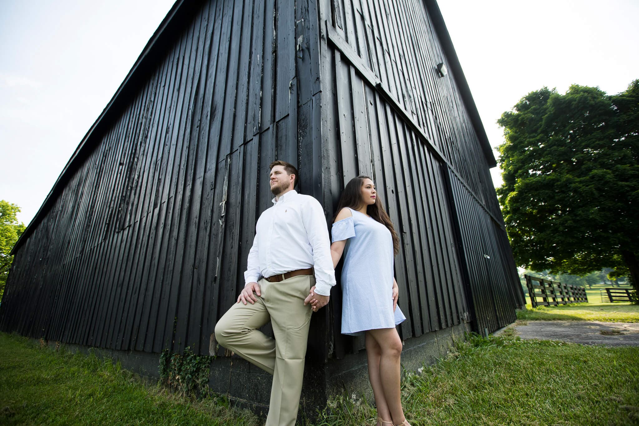 An engaged couple standing at the corner of a barn looking separate ways.